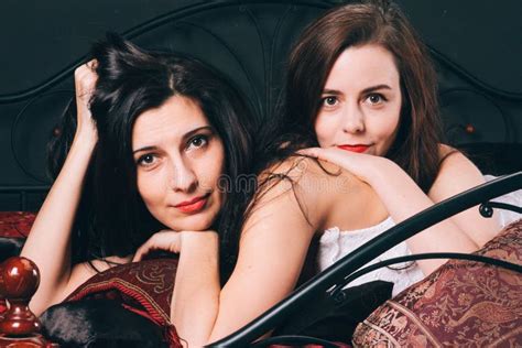 Deux Jeunes Femmes Dans La Lingerie De Cru Sur Le Lit écarté Contre Le Mur Noir Jeux D amour