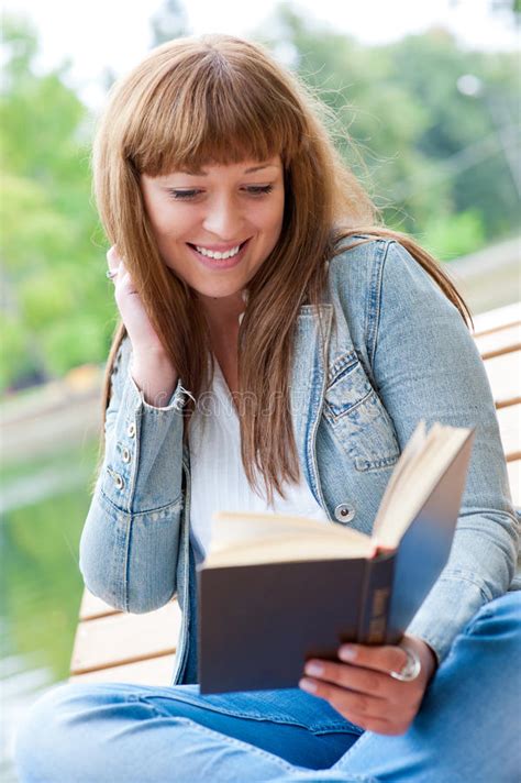 Mulher Nova Que Lê Um Livro Que Senta se No Banco Foto de Stock