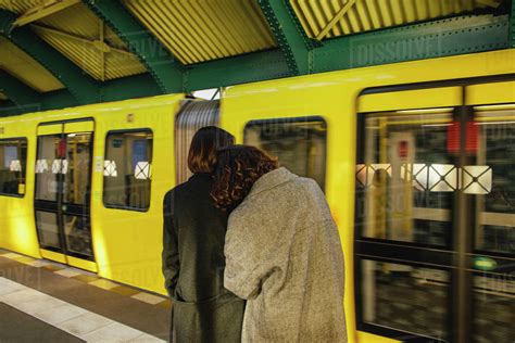 Rear View Of Lesbian Couple Standing At Railroad Station Against Yellow