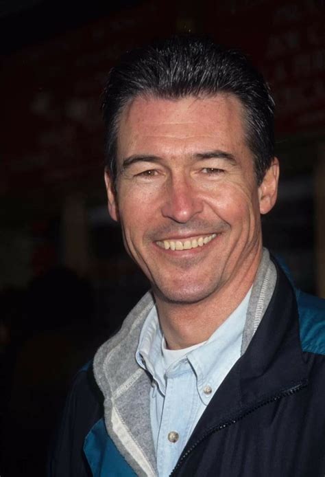 A Smiling Man Wearing A Jacket And Blue Shirt