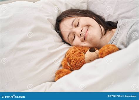 Young Woman With Down Syndrome Lying On Bed Sleeping With Teddy Bear At