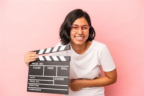 Joven latina sosteniendo claqueta aislado sobre fondo rosa riendo y divirtiéndose Foto Premium