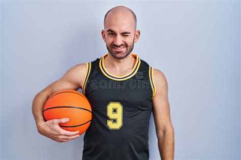 Young Bald Man With Beard Wearing Basketball Uniform Holding Ball