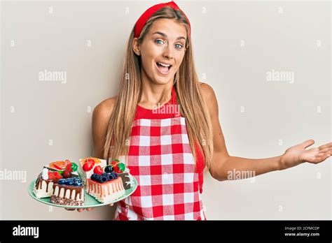 Junge blonde Frau trägt Bäcker Uniform hält hausgemachte Kuchen feiern Leistung mit glücklichen