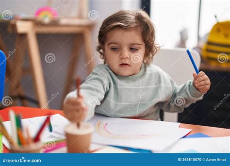 Adorable Hispanic Girl Student Sitting On Table Drawing On Paper At