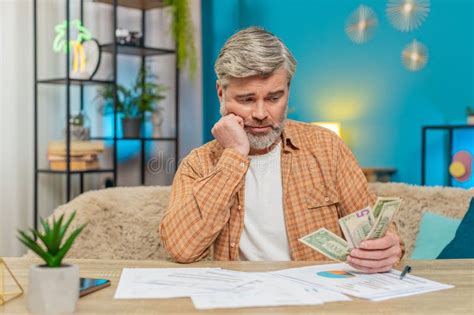 Mature Man At Table With Documents Bills Holding Money Cash Showing Financial Distress At Home