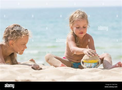 Two Girls On The Beach On A Sunny Day Playing With Sand And A Bucket