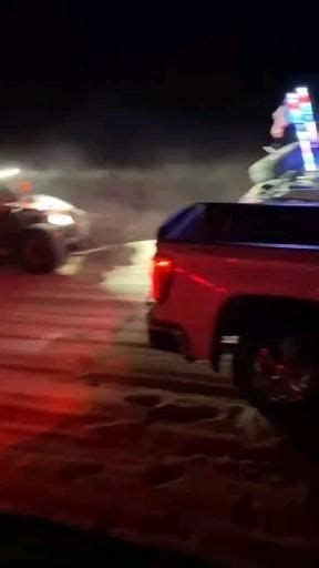 Two Police Cars Driving Down A Street At Night