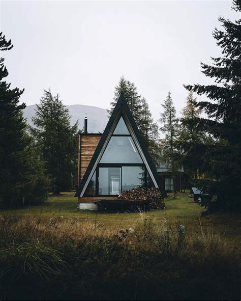 A House In The Middle Of Some Trees And Grass With Mountains In The