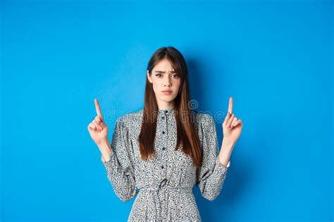 Hesitant And Worried Young Woman Frowning Pointing Fingers Up With Sad