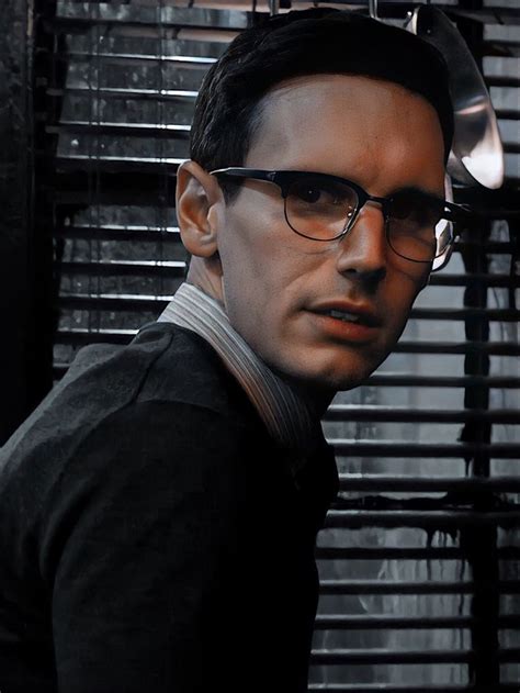 A Man Wearing Glasses Standing In Front Of A Window With Blinds On The