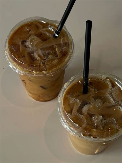 Two Plastic Cups Filled With Ice Cream And Brown Liquid Sitting Next To