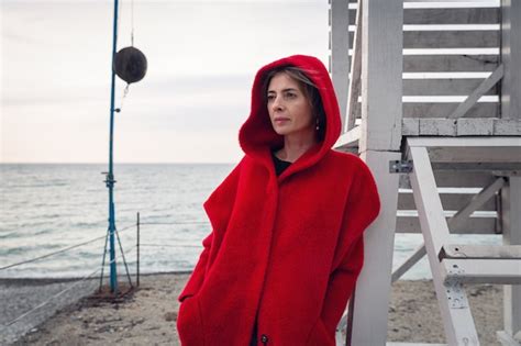 Premium Photo A Woman In Red Coat Stands On The Seashore Leaning