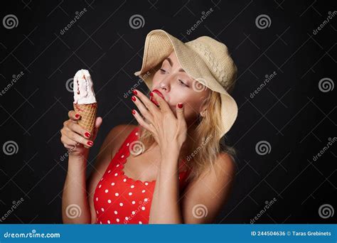 Stunning Blonde European Woman In Summer Straw Hat And Red Swimsuit Provocatively Eating A