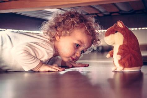 Funny Cute Curious Baby Playing Under The Bed With Toy Hamster In