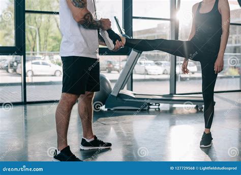 Male Personal Trainer Helping Sportswoman To Stretching At Gym Stock