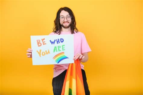 Jeune homme gay souriant bisexuel queer avec maquillage en chemise de réservoir beige tenir