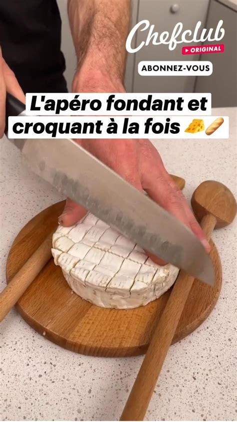 A Man Is Cutting Cheese On A Wooden Board With A Knife In His Hand And