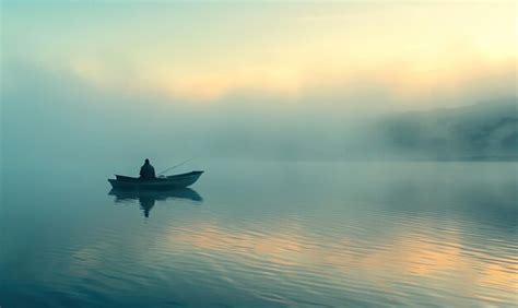 Small Fishing Boat On A Misty Lake At Twilight With A Lone Fisherman