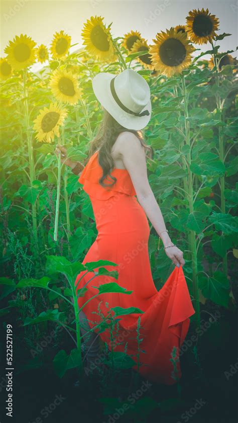 Mujer Con Sombrero Blanco Y Vestido Naranja Oliendo Un Girasol En Medio