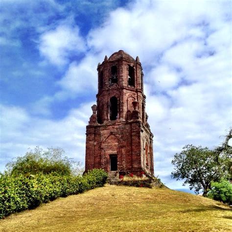 A Very Tall Tower Sitting On Top Of A Lush Green Hillside Under A