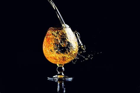 Бокал с коньяком с брызгами на черном фоне | Премиум Фото