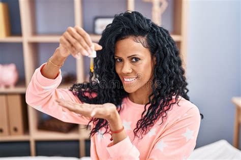 African American Woman Pouring Serum Lotion On Hand Sitting On Bed At