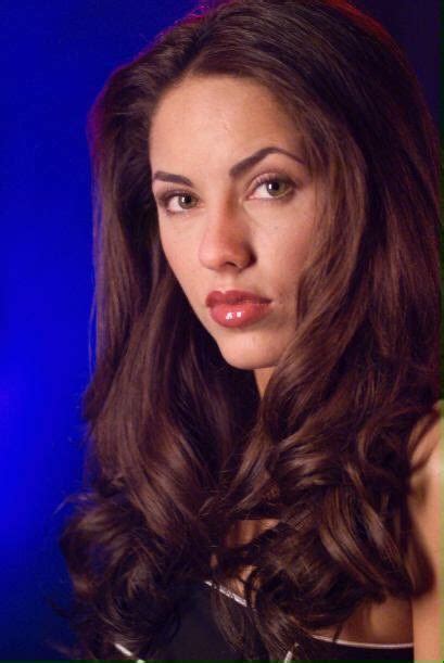 A Woman With Long Dark Brown Hair Posing For A Photo In Front Of A Blue