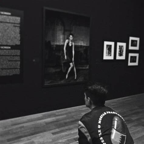 A Man Sitting On The Floor In Front Of A Wall With Pictures Hanging On It