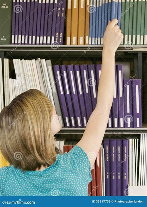 Young Woman Reaching For Book From Library Shelf Stock Photo Image Of