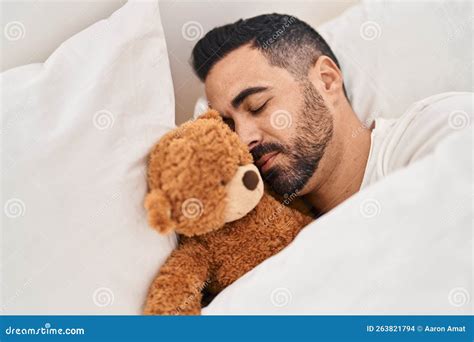 Young Hispanic Man Lying On Bed Sleeping With Teddy Bear At Bedroom