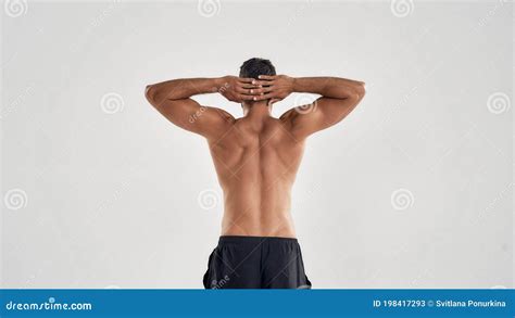 Back View Of Muscular Man With Naked Torso Keeping Arms Over The Head Over Grey Background