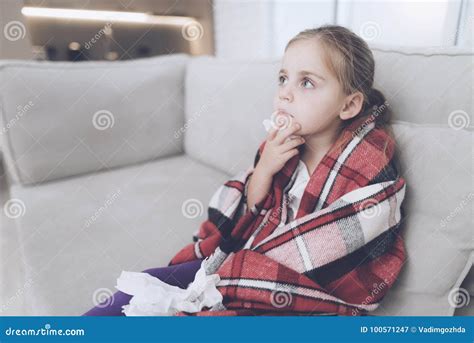 Little Sick Girl Sits On A White Couch Wrapped In A Red Scarf She Is Cold And She Wrapped