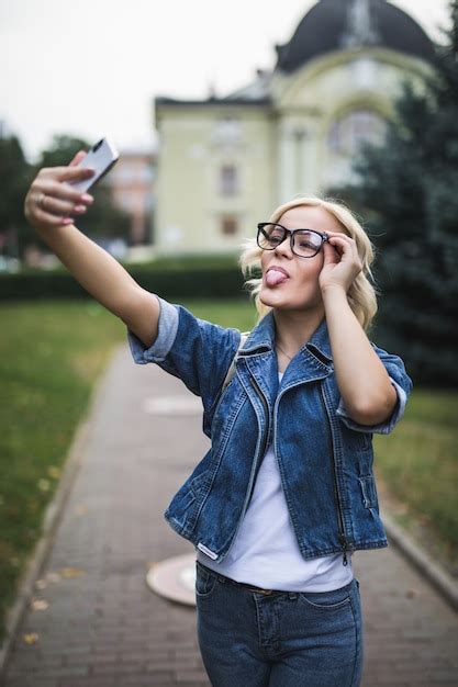 Mode élégante Fille Blonde Femme En Suite De Jeans Et Lunettes Fait Selfie Sur Son Téléphone