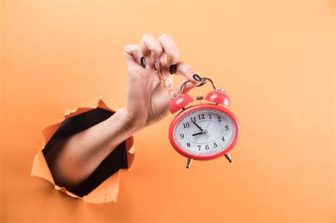 Premium Photo Female Hand Holding Alarm Clock On Orange Background