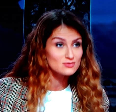 A Woman With Long Curly Hair Wearing A Blazer And White Shirt Is