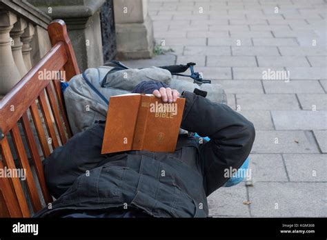 A Homeless Man In Edinburgh Relaxing On A Public Bench Reading The