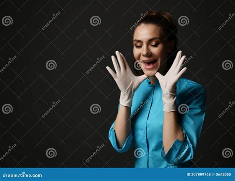 Young Brunette Woman Doctor Nurse In Blue Medical Gown And Latex Gloves Holds Hands At Face