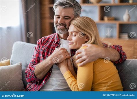 Smiling Mature European Husband Embracing Wife Enjoy Comfort And Romance Sit On Sofa In Cozy