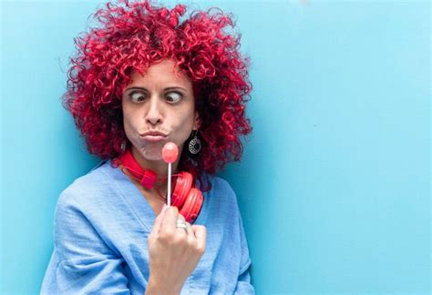 Una Mujer Latina Con Un Pelo Afro Rojo Sobre Fondo Azul Con Ojos Viscosos Mirando Chupa Chups