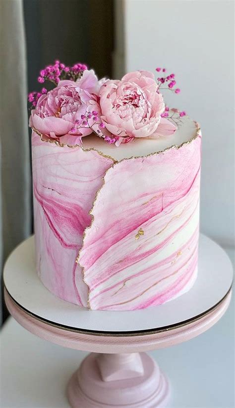 A Pink Marbled Cake With Flowers On Top Is Sitting On A White Plate And