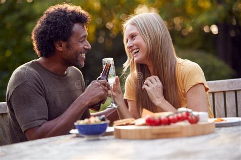 Mature Couple Celebrating With Beer And Champagne As They Sit At Table In Garden With Snacks