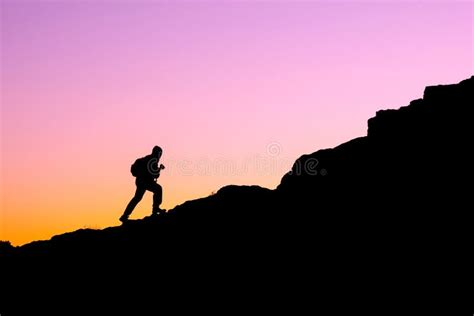 The Silhouette Of A Man Climbing A Mountain In The Sunset Light Stock