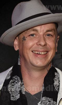 a man with tattoos on his face wearing a white hat and scarf smiling at ...