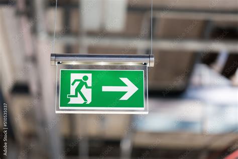Illuminated emergency exit sign, hanging from the ceiling. With running ...