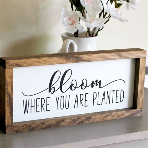 A Wooden Sign That Says Bloom Where You Are Planted Next To A Vase With