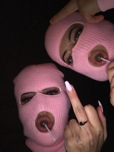 Two Women Wearing Pink Masks With One Pointing At The Other S Nose And