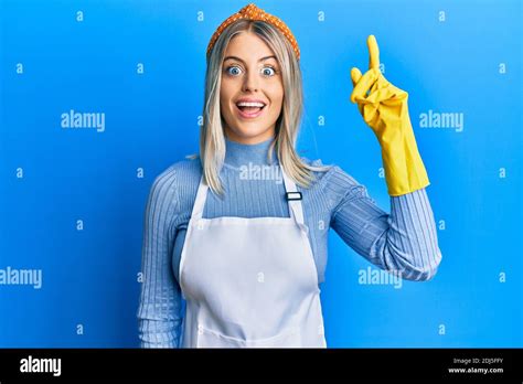 Belle Femme Blonde Portant Un Tablier Plus Propre Et Des Gants Pointant Le Doigt Vers Le Haut
