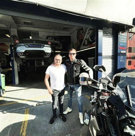 Two Men Standing Next To Each Other In Front Of A Motorcycle