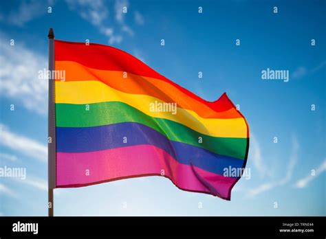Gay Pride Rainbow Flag Fluttering Backlit In The Sun Against Soft Blue Sky Copy Space Stock